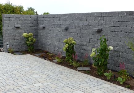 Steinmauer an Hofeinfahrt mit bepflanztem Grünstreifen