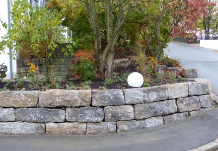 Natursteinmauer mit Gehölz an Straßenecke